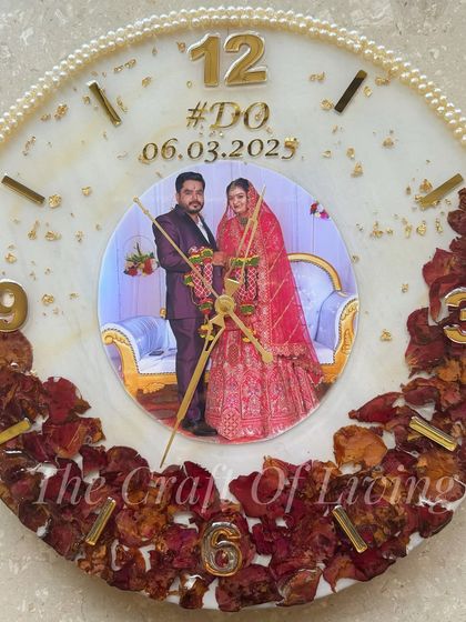 A vibrant wall clock with a large central photo, surrounded by preserved red rose petals. The mix of standard and numerical hour markers gives it a modern feel.
