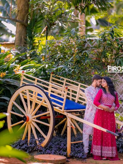 A couple in traditional attire poses with a rustic bullock cart prop, a unique element that adds a touch of village charm to the garden setting.