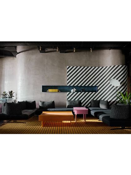 A lounge area defined by a bold, black-and-white diagonally striped wall. The low-slung modular sofa and pops of pink and wood create a graphic, contemporary look.