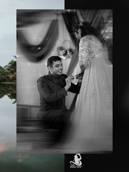 A classic and timeless black and white photo of the groom-to-be on one knee, placing the ring on his partner's finger during their engagement.