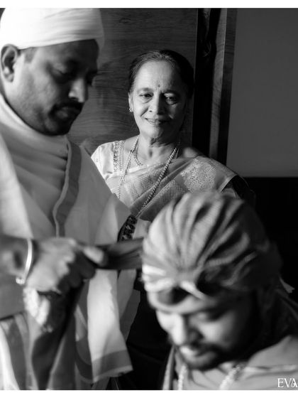 A poignant black and white photo of a mother looking on with love as her son participates in the wedding rituals.