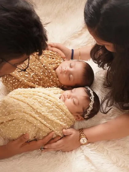 An intimate overhead shot of parents lovingly gazing at their newborn twins, who are swaddled peacefully together on a soft, fluffy blanket.