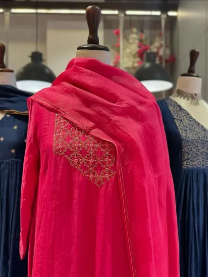 A focus on the fuchsia pink anarkali, with its simple gold embroidered patch adding a touch of elegance to the vibrant fabric.