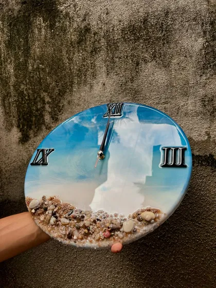 This close-up shot of the ocean wall clock highlights the glossy, mirror-like finish and the texture of the embedded shells. It's a piece that invites you to look closer.
