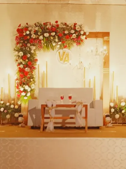 A chic and modern wedding stage in red and white, featuring an asymmetrical floral arch, minimalist furniture, and ambient candle lighting for a romantic feel.