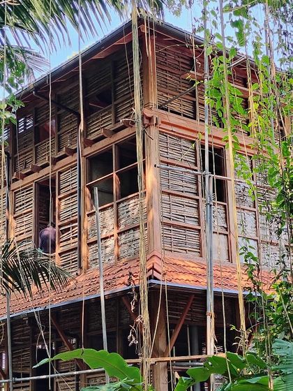 A craftsman works on the woven bamboo panels of the cottage during construction. This highlights the handcrafted process behind the prefab system.