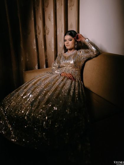 The bride, Garvita, seated in a glamorous, shimmering gown. The low-light setting and her relaxed pose create a portrait that is both sophisticated and modern.