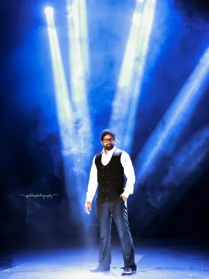 A formal and dramatic series of a model in a black sherwani. The shots are taken in unique studio settings, one with dramatic blue spotlights and another with a wall of chandeliers, creating a high-end, luxurious feel.