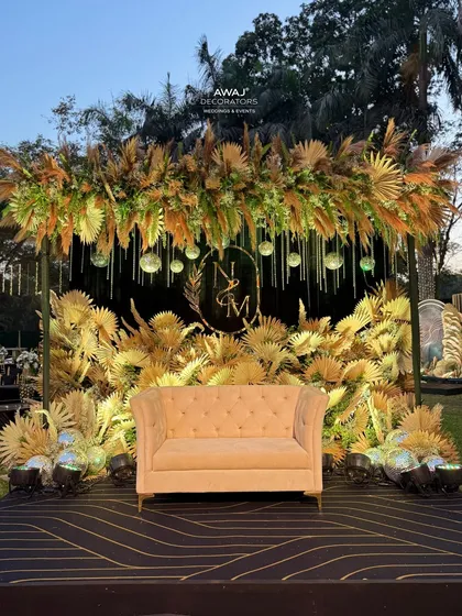 Showcasing a chic, rustic sangeet stage design that blends natural pampas grass with a custom couple's monogram and soft lighting, perfect for a stylish and contemporary celebration.