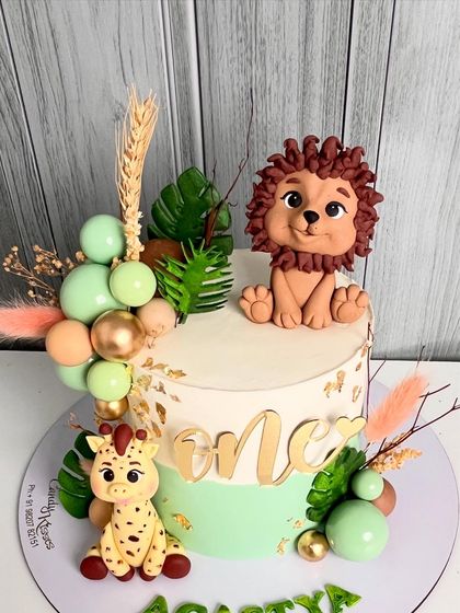 An adorable jungle-themed cake for a first birthday, featuring a hand-sculpted lion and giraffe, accented with pastel green and gold details, and dried botanicals.