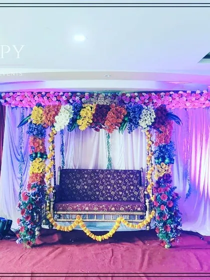 A colorful swing (jhula) decoration for a baby shower or Dohale Jevan ceremony. The swing is framed with multi-colored flowers, creating a joyful and festive look.