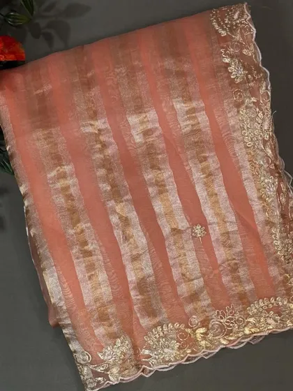 A close-up of the peach tissue stripes organza saree, highlighting the delicate embroidery and scalloped edge.