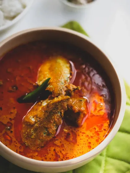 A vibrant chicken or fish curry, its deep red color indicating a rich blend of chilies and spices, typical of many regional Indian cuisines.