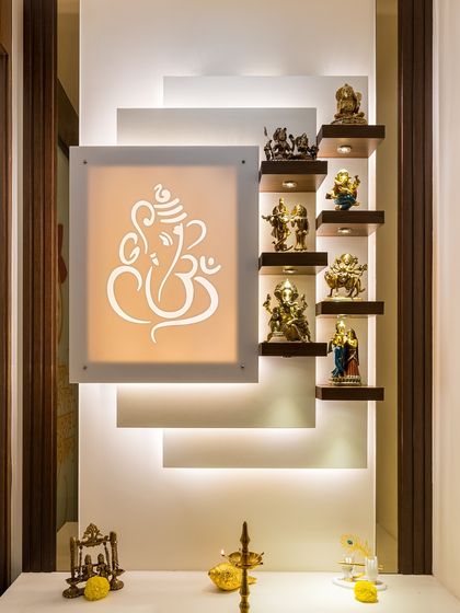 A modern and minimalist pooja wall featuring a backlit Ganesha etching and staggered floating shelves for various idols. The clean lines and focused lighting create a space that is both spiritual and stylish.