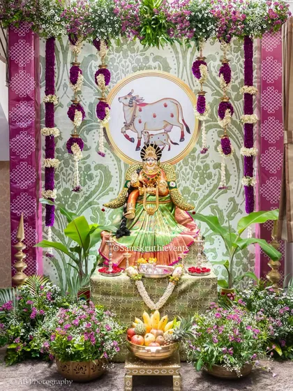 A divine setup for a Varalakshmi festival. We decorated the goddess with rich fabrics and fresh flowers, set against a backdrop featuring Kamadhenu motifs and surrounded by lush greenery to create a truly sacred space.