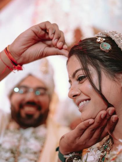 The groom applies sindoor to the bride's forehead, a beautiful and significant ritual captured with a focus on the bride's happy expression.