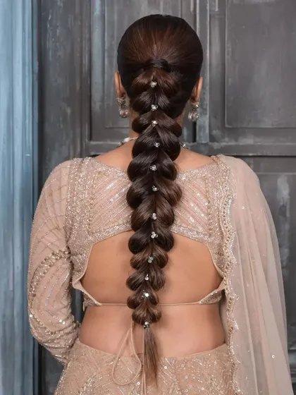 A detailed view of a clean, pull-through braid accented with delicate pearls. This hairstyle offers a modern and refined look, perfect for sangeet or cocktail event styling in a campaign shoot.