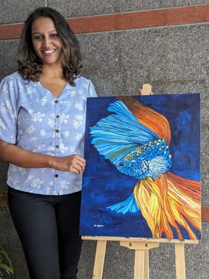 Sindhu shows off her completed acrylic painting of a vibrant betta fish. This project focused on capturing the fluid movement and iridescent colors of the fish's fins.