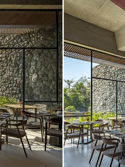 The dining area at the Radisson Resort is framed by large windows that look out onto a curved stone wall and lush greenery. This visual connection unifies the interior and exterior spaces, making the landscape a part of the dining experience.