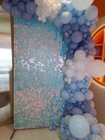 A magical Disney Princess theme for a fourth birthday. This setup features a shimmering sequin wall in iridescent blue, framed by a balloon garland in shades of blue and white, creating a frozen, icy feel perfect for a little queen.