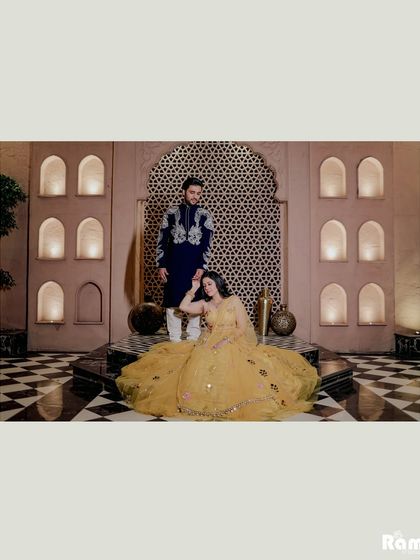 A majestic portrait set in a room with intricate jaali work and a checkered floor. The bride's yellow lehenga spreads out beautifully, creating a stunning composition full of royal vibes.