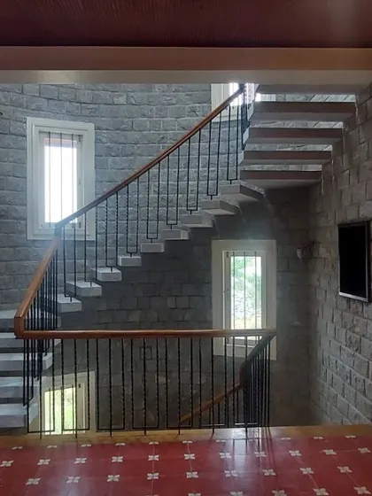 A floating staircase against a backdrop of stone walls, with red oxide flooring adding a splash of color.