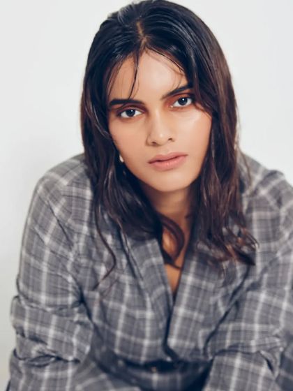 A simple, direct portrait showcasing the modern, androgynous feel of the plaid blazer and wet-look hair. The makeup is kept clean and minimal to let the styling and model's expression shine.