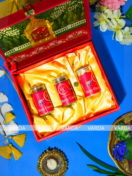 A luxurious red and gold gift box designed for wedding favors. The interior, lined with golden satin, holds three jars of flavored nuts, while the lid features a custom monogram and traditional elephant artwork.