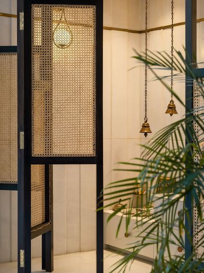 A sacred prayer space (puja room) designed with modern sensibilities. The use of traditional cane screens, brass bells, and soft lighting creates a tranquil atmosphere that feels both contemporary and reverent.