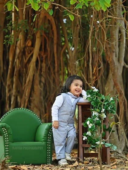 A sweet, smiling portrait of the boy in his suit, leaning against a prop in a natural, wooded setting.