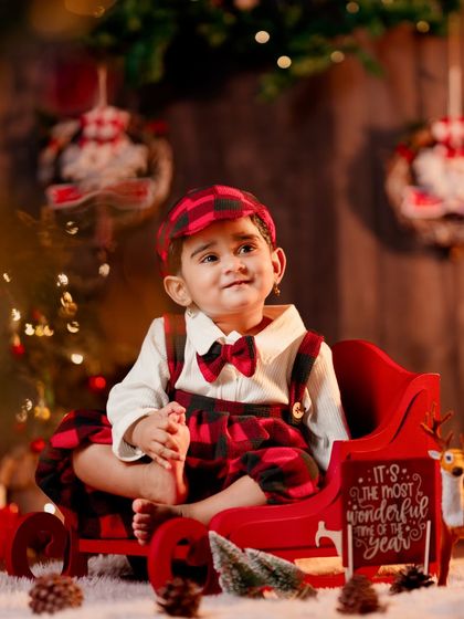 A dapper little gentleman in his Christmas best, sitting in a red sleigh and looking up with wonder.