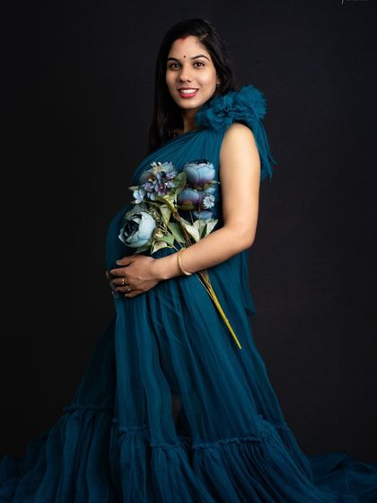 A beautiful smile that lights up the room. Dressed in a stunning teal gown and holding flowers, she looks absolutely radiant and full of joy.