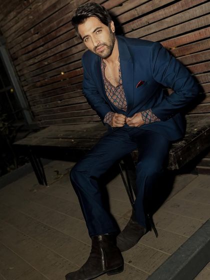 This seated pose is more direct and confident, showcasing the stylish suit in a relaxed, outdoor setting.