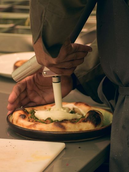 Using a siphon to add a potato parmesan espuma to a jackfruit flatbread. This elevates a rustic dish with a touch of modern gastronomy.