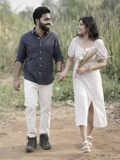 A happy couple walks hand-in-hand down a country path, the bride holding a small bouquet, creating a lovely, candid photo.