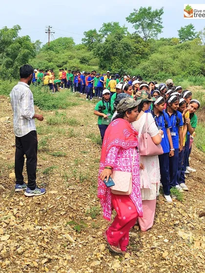 A long line of students and teachers walking along the plantation site. It takes a large, coordinated effort to plant thousands of saplings in a day.