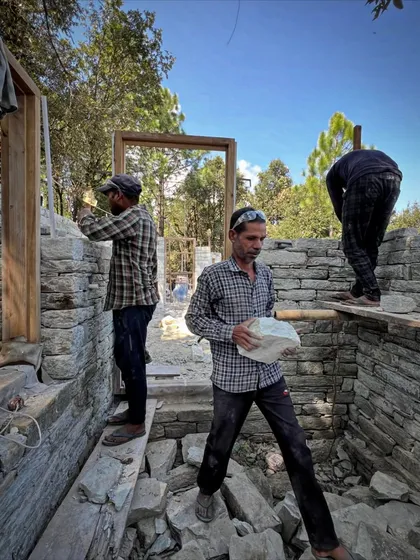 Artisans work together on the stone walls of a guesthouse. Building in the Himalayas is a testament to teamwork, with each craftsperson bringing their unique skills to the collective effort.