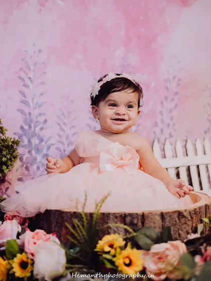 A happy baby girl smiling brightly, surrounded by flowers in a whimsical, garden-themed studio setup. Capturing these joyful expressions is the goal of every baby session.