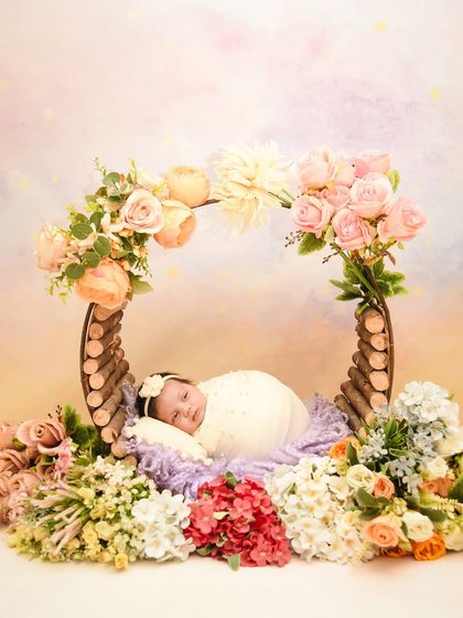 A baby rests in a rustic wooden prop adorned with a colorful mix of flowers. This setup creates a vibrant, garden-like feel for the newborn portrait.