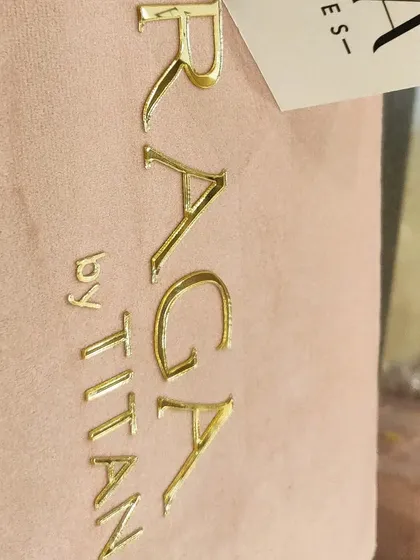 A close-up of the gold foil branding on a pastel pink suede watch box, created for the Titan Raga collection in collaboration with Alia Bhatt. The luxurious texture and finish reflect the premium quality of the brand.