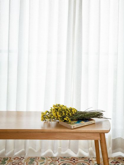 Serenity in simplicity. A simple wooden bench against a backdrop of sheer curtains and a bouquet of fresh flowers creates a moment of pure, understated beauty.
