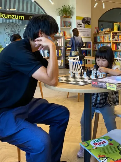 A father and daughter locked in a serious game of chess. Our space is designed for more than just reading; it's for play, strategy, and fun.
