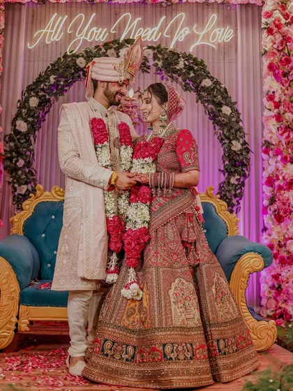 The quintessential grand wedding shot. The couple stands together under a "All You Need Is Love" neon sign, perfectly capturing the celebratory and romantic spirit of their big day.