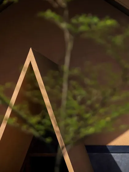 A detail of the A-frame architectural motif at Teyla, seen through the foliage of a nearby tree, emphasizing the project's connection to its natural setting.