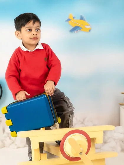 Ready for takeoff. This little traveler is holding his suitcase, ready to board his wooden airplane in this adventurous studio setup.