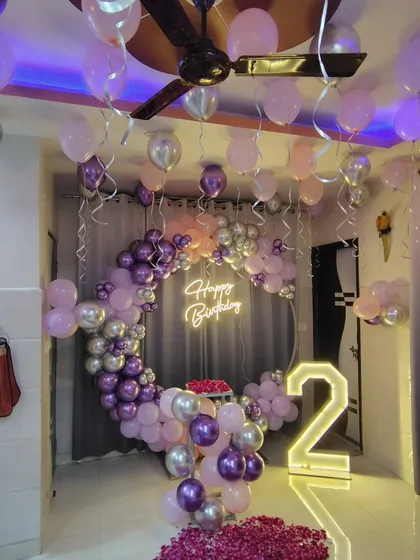 A wider view of the purple-themed birthday party, showing balloons on the ceiling and a rose petal carpet.