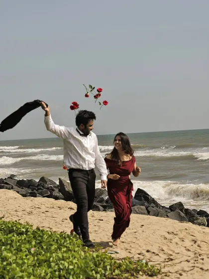 A playful and romantic moment on the beach, with the groom tossing roses in the air as they walk by the sea. This captures a feeling of joy and celebration.