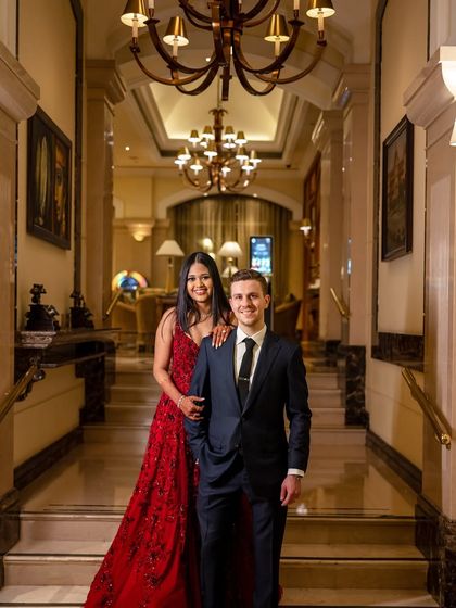 A sophisticated couple poses in a grand hotel lobby. We styled the bride in a stunning red gown with flowing hair and glamorous makeup for her reception, while the groom looks sharp in a classic suit.
