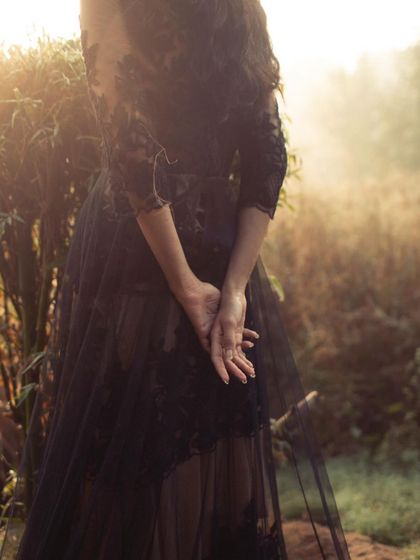 A detail shot from a moody, black-and-white editorial. The focus is on the delicate lace and sheer tulle of the gown, with the soft, hazy light creating a romantic and mysterious atmosphere.