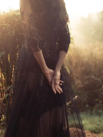 A detail shot from a moody, black-and-white editorial. The focus is on the delicate lace and sheer tulle of the gown, with the soft, hazy light creating a romantic and mysterious atmosphere.